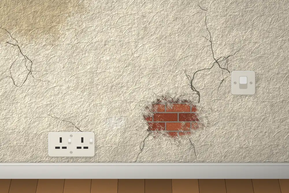 Before: an old artex swirl wall with long cracks, a damp stain and a hole showing the brickwork.